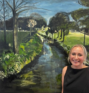 Rebecca J Spence standing in front of one of her landscape paintings